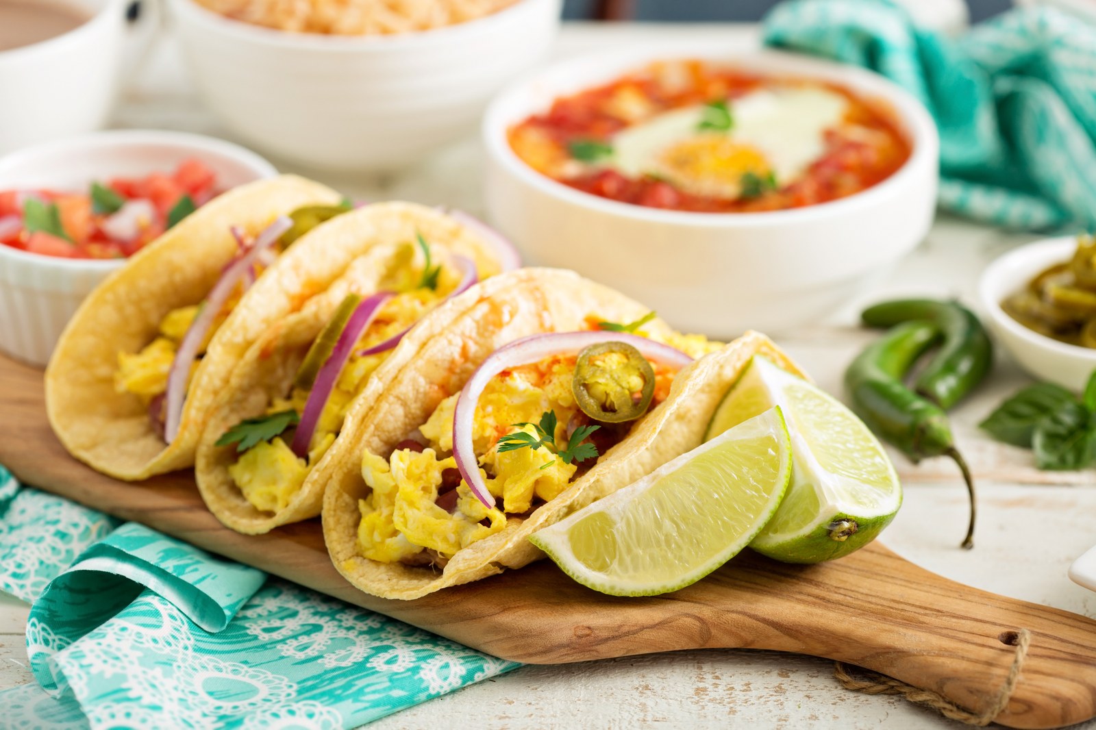 Breakfast tacos filled with scrambled eggs and potatoes on corn tortillas with lime wedges and jalapeños