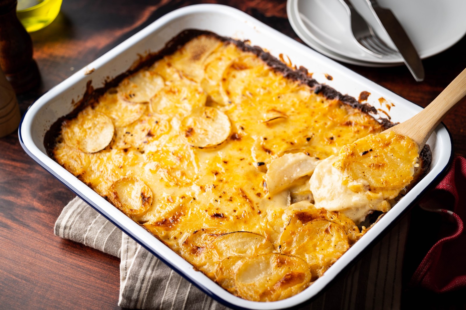 Baked potato gratin in a white dish with golden, bubbly cheese topping and layered potato slices visible