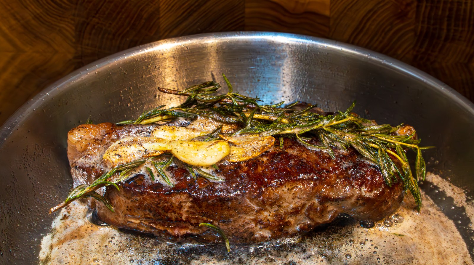 Ribeye steak sizzling in a cast iron skillet topped with garlic slices and fresh rosemary