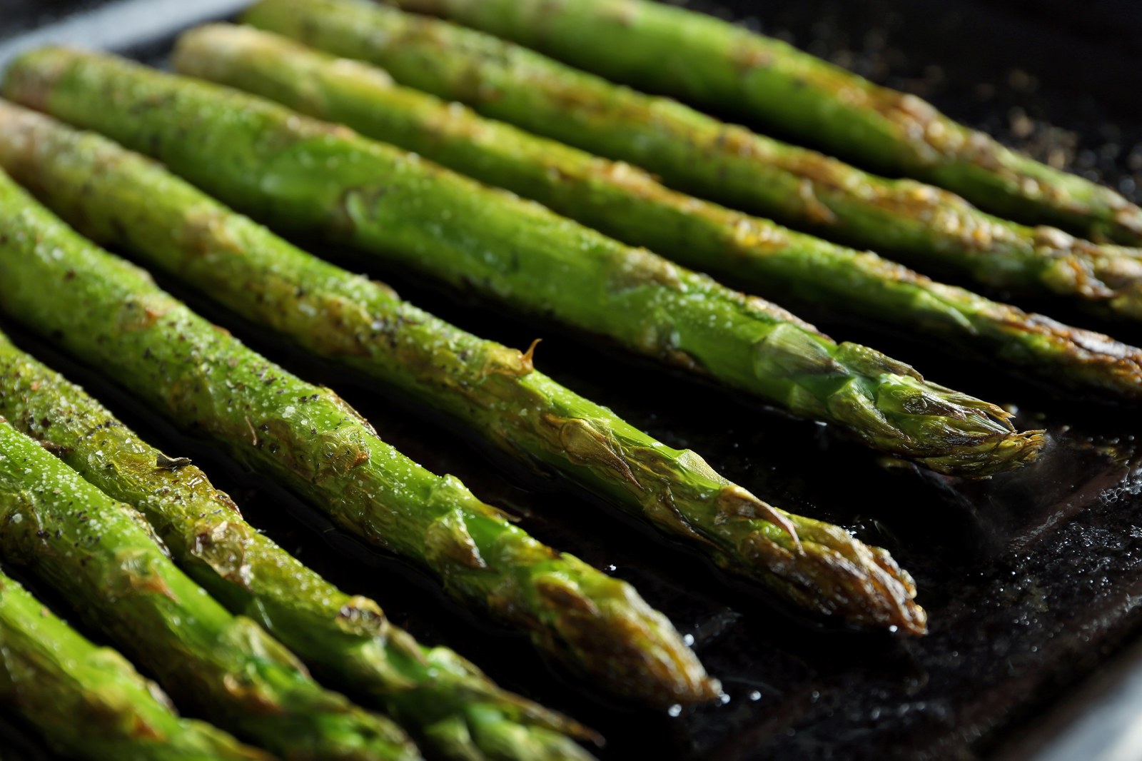 Fresh asparagus spears roasted until tender with lightly charred tips on a dark surface