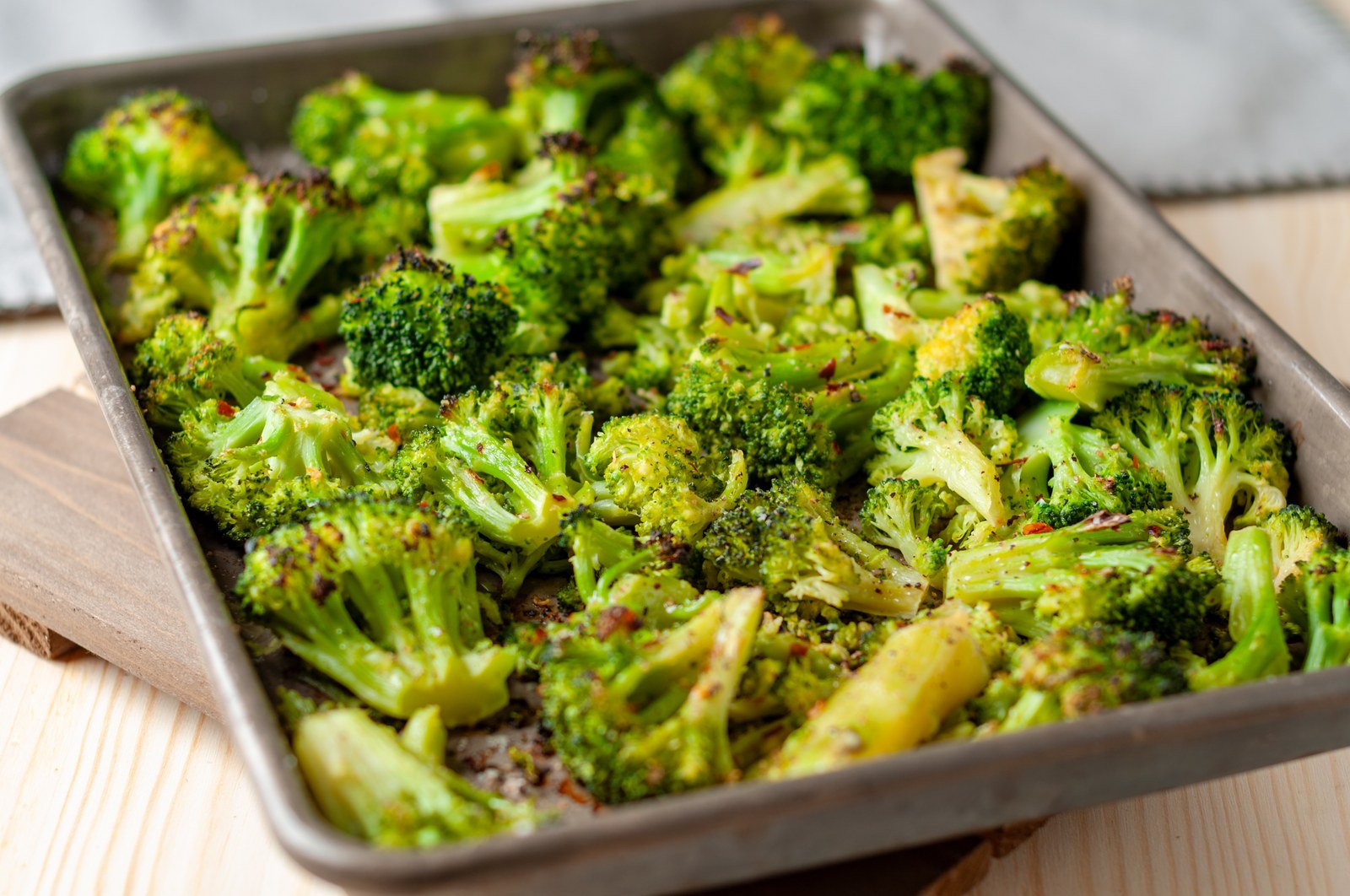 Baking sheet of roasted broccoli florets with golden brown edges and light char marks