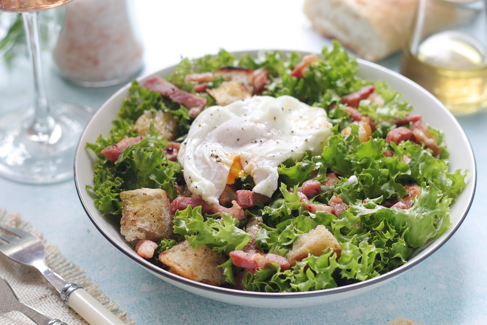 French salad with frisée lettuce, crispy bacon lardons, croutons, and a poached egg on top