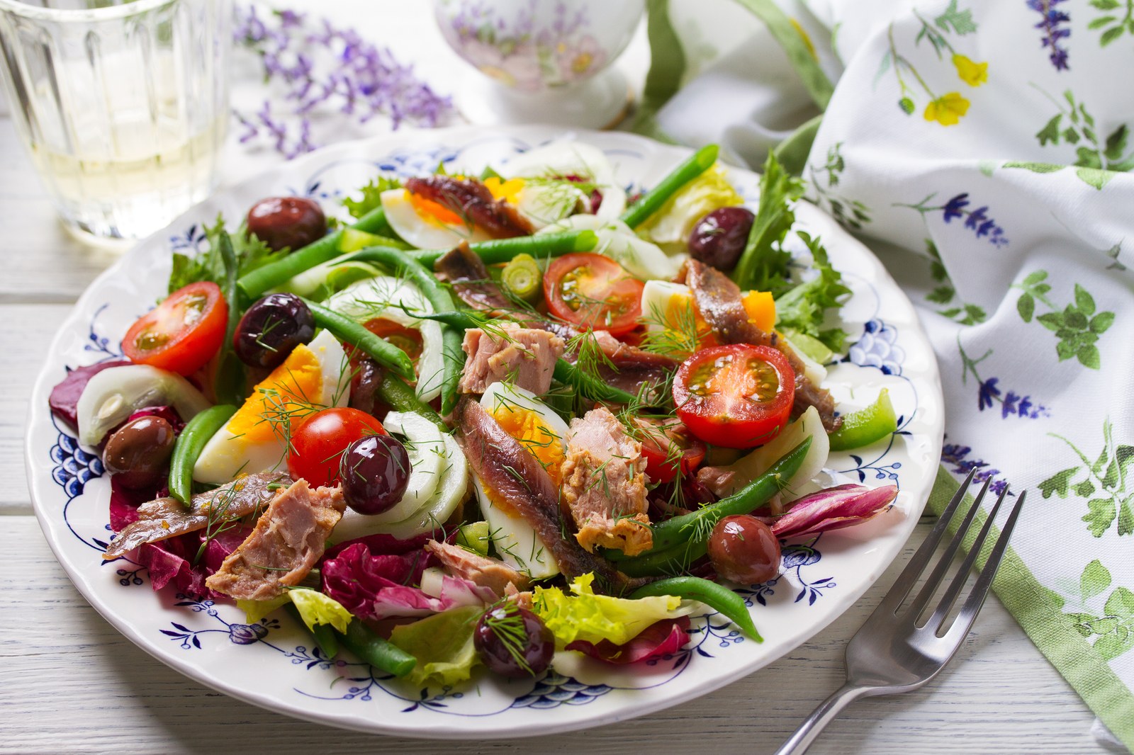Colorful Niçoise salad with tuna, hard boiled eggs, green beans, tomatoes, olives, and fresh herbs
