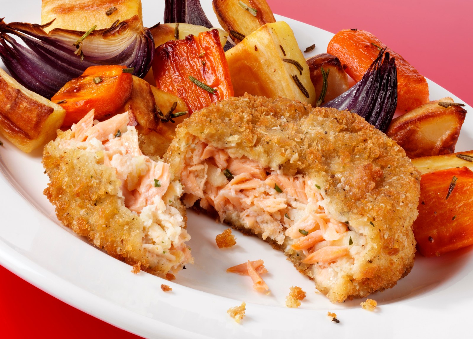 Breaded salmon cakes cut open to show flaky interior, served with roasted vegetables
