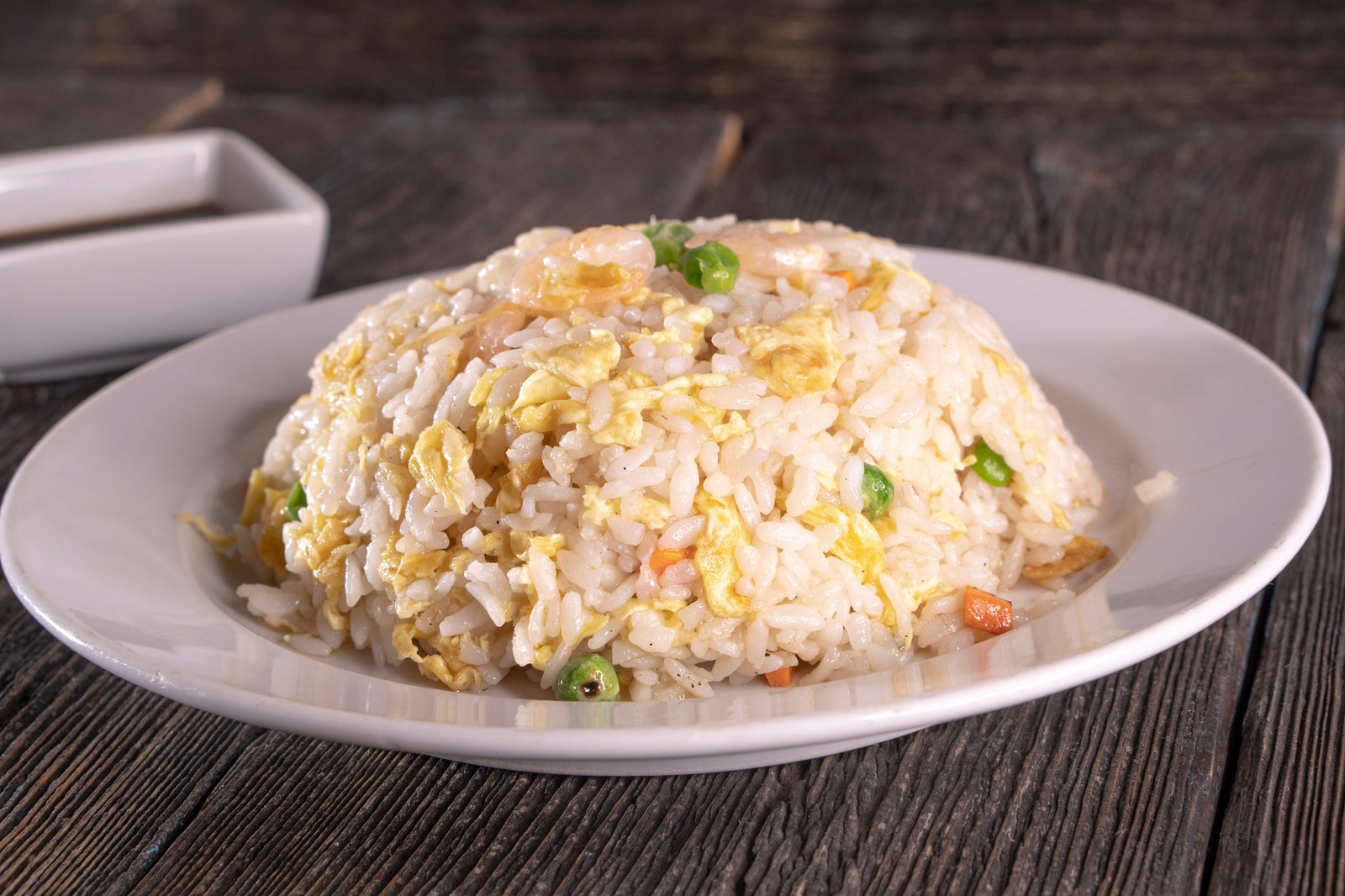 A mound of fried rice with scrambled eggs, green peas, and diced vegetables on a white plate with chopsticks nearby