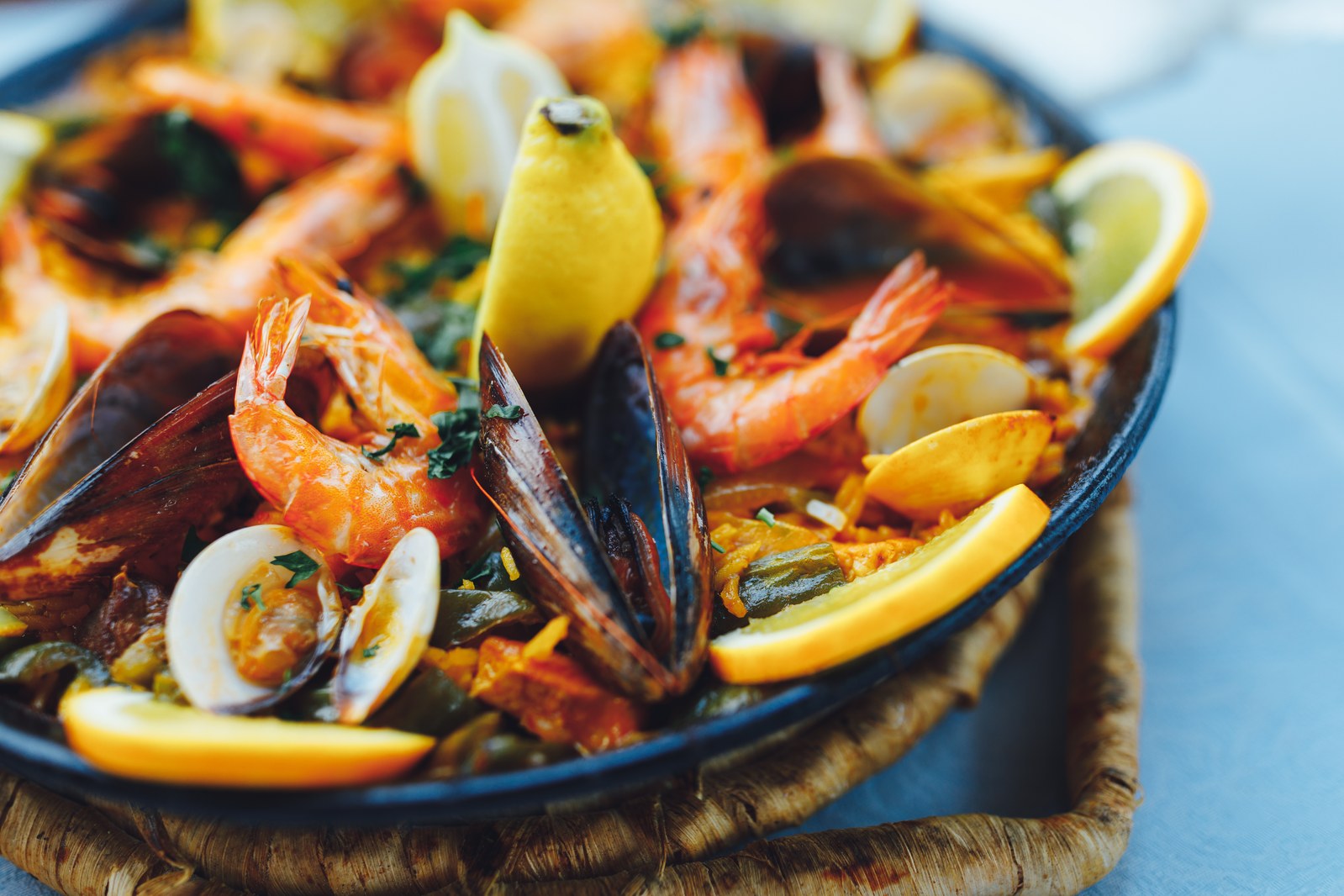 Traditional Spanish paella in a black pan filled with saffron rice, pink shrimp, black mussels, white clams, and lemon wedges
