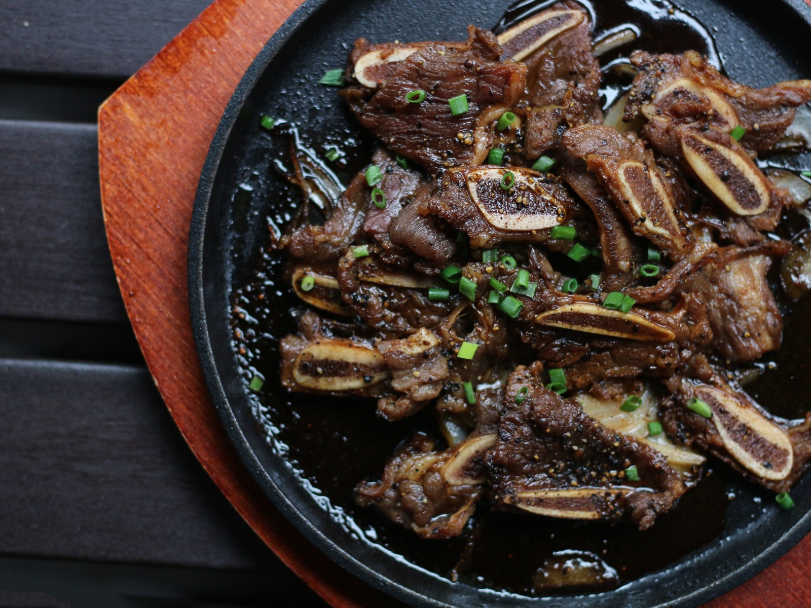 Korean style grilled short ribs with charred edges and sliced onions in a black cast iron skillet garnished with sesame seeds and green onions
