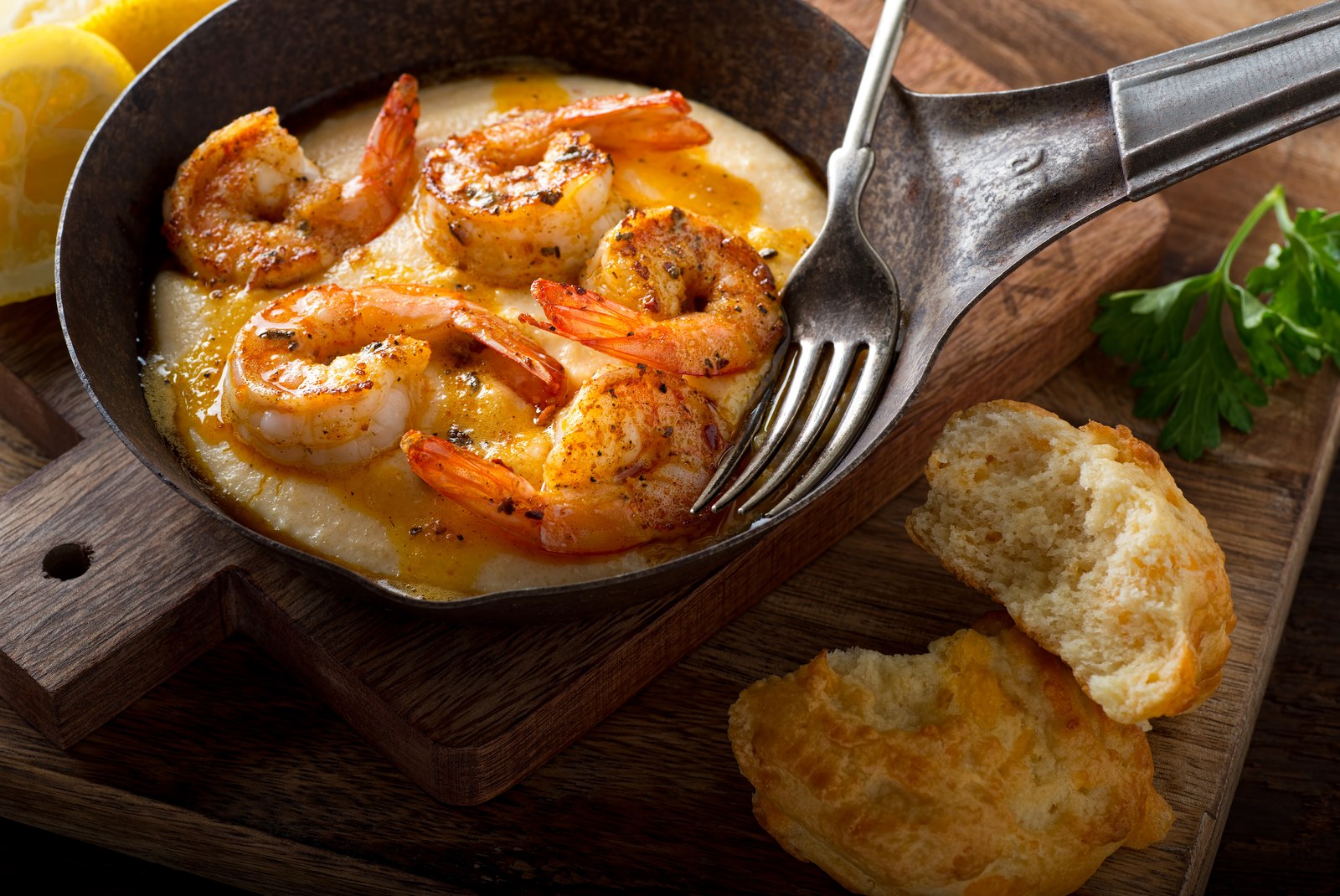 Several large seasoned shrimp nestled in creamy yellow cheese grits in a black cast iron skillet with bread slices on the side