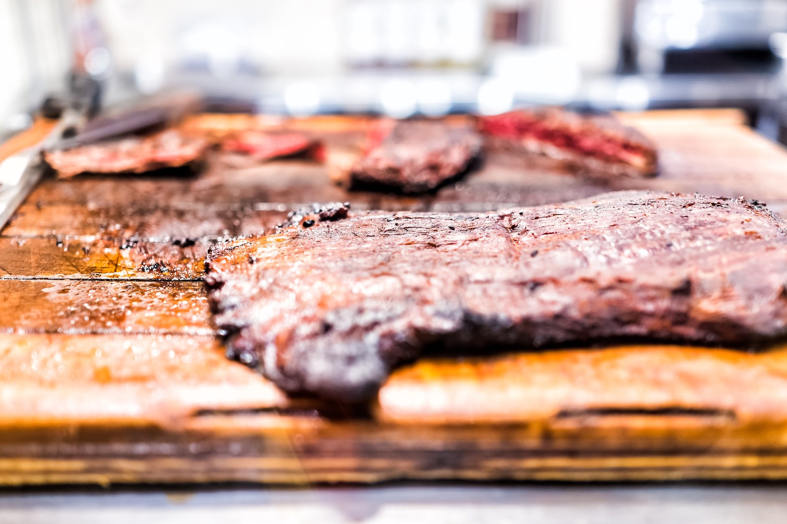 Multiple pieces of marinated grilled skirt steak resting on a wooden cutting board, showing charred exterior and pink juicy interior