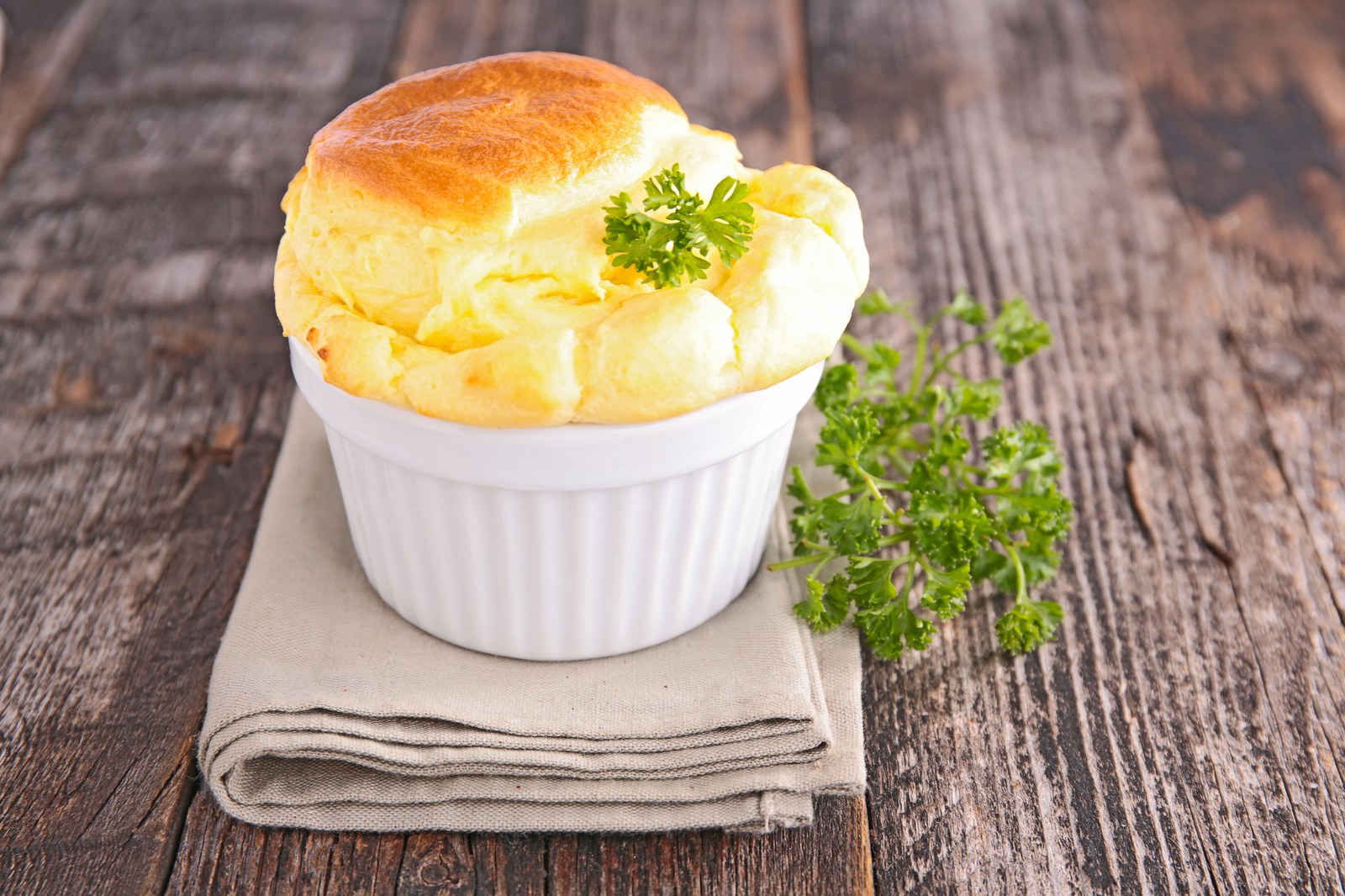 A risen soufflé in a white ramekin, garnished with parsley