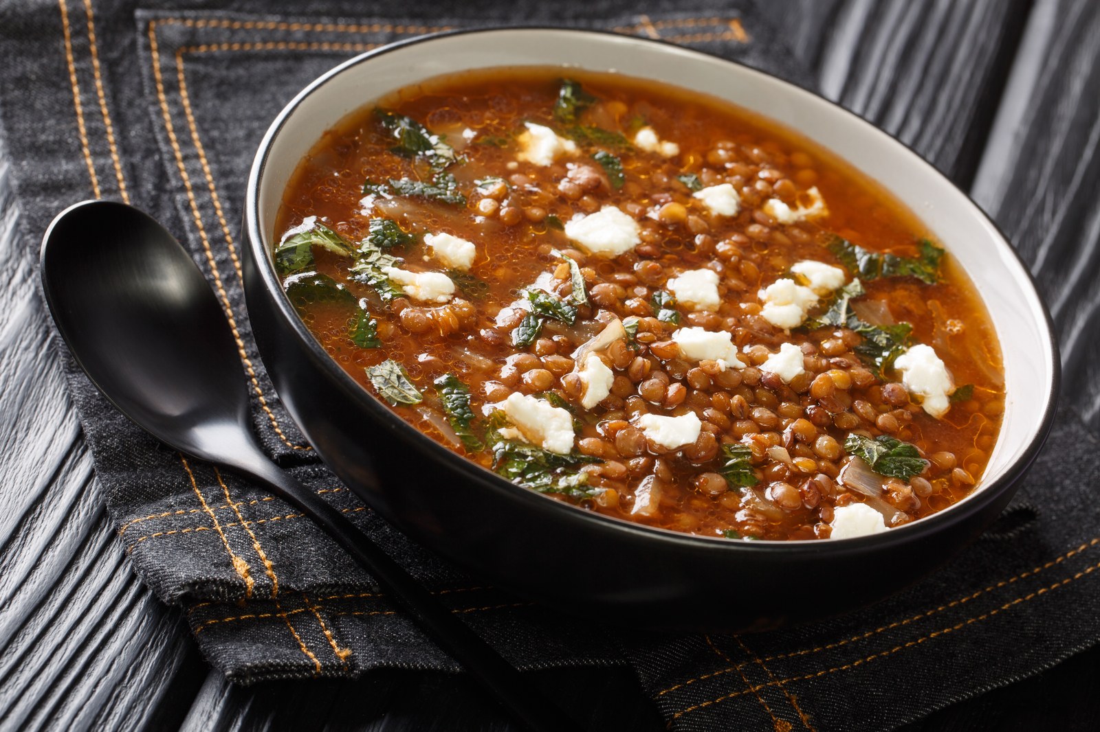 Greek lentil soup in a black bowl topped with feta cheese and herbs
