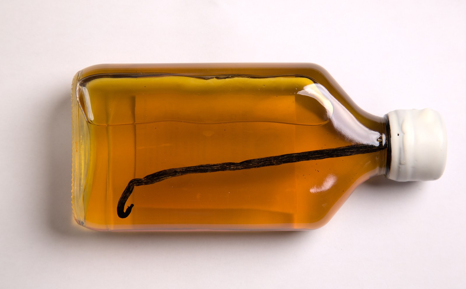 A clear glass bottle filled with amber maple syrup with a vanilla bean visible inside