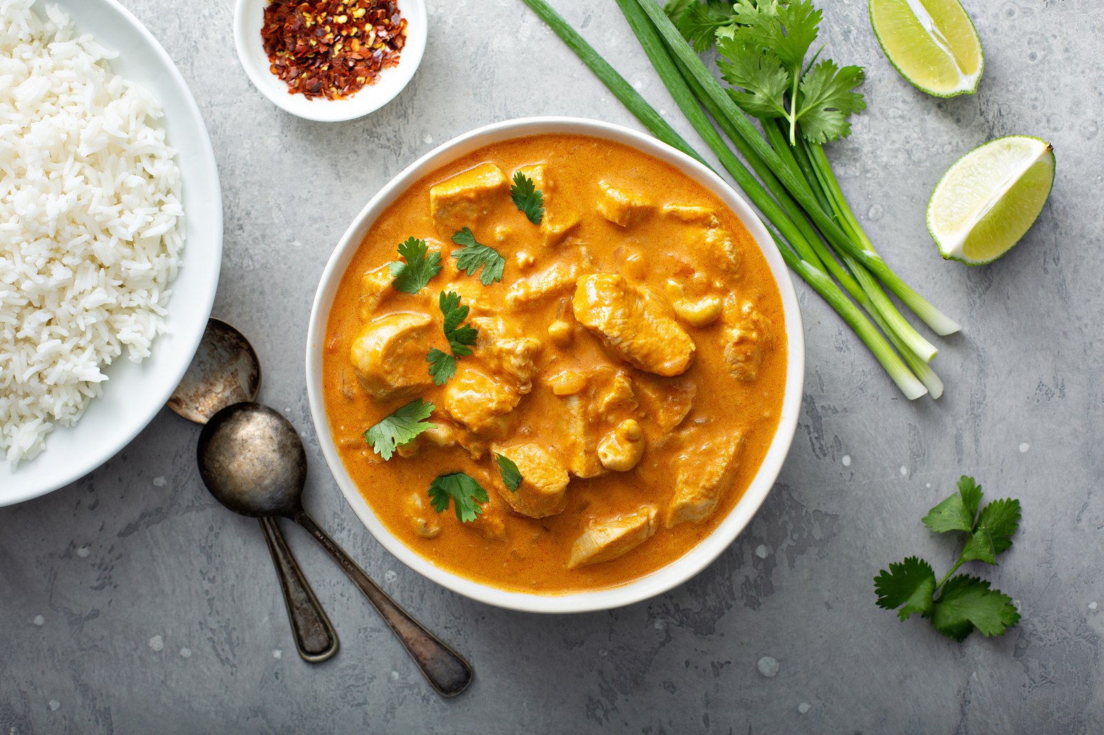 Thai red curry with chicken pieces in rich orange-red coconut sauce, garnished with cilantro, red chilies, served with jasmine rice