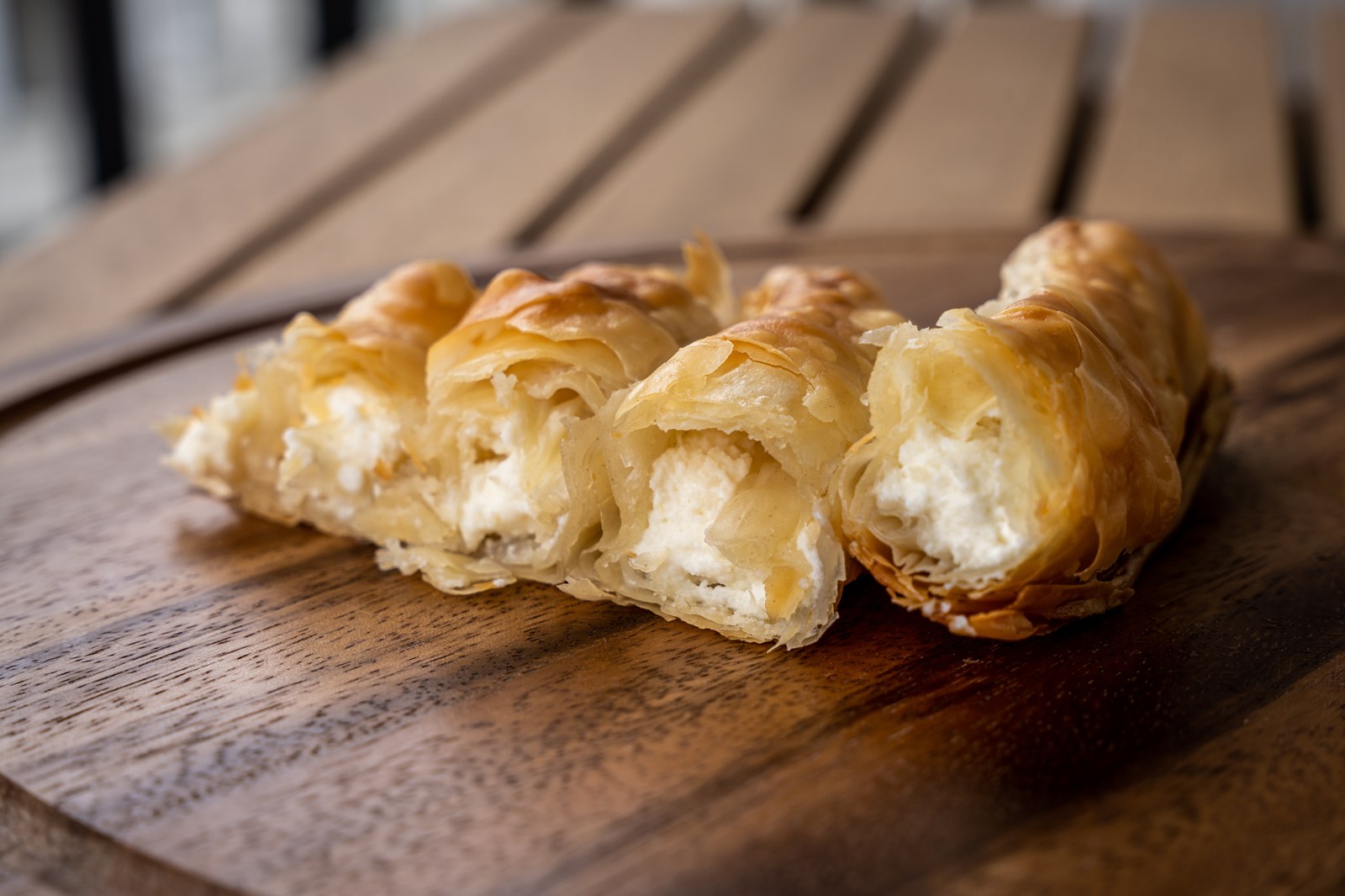 Greek tiropita cheese rolls with flaky golden phyllo pastry layers, white feta cheese filling visible at ends on wooden board