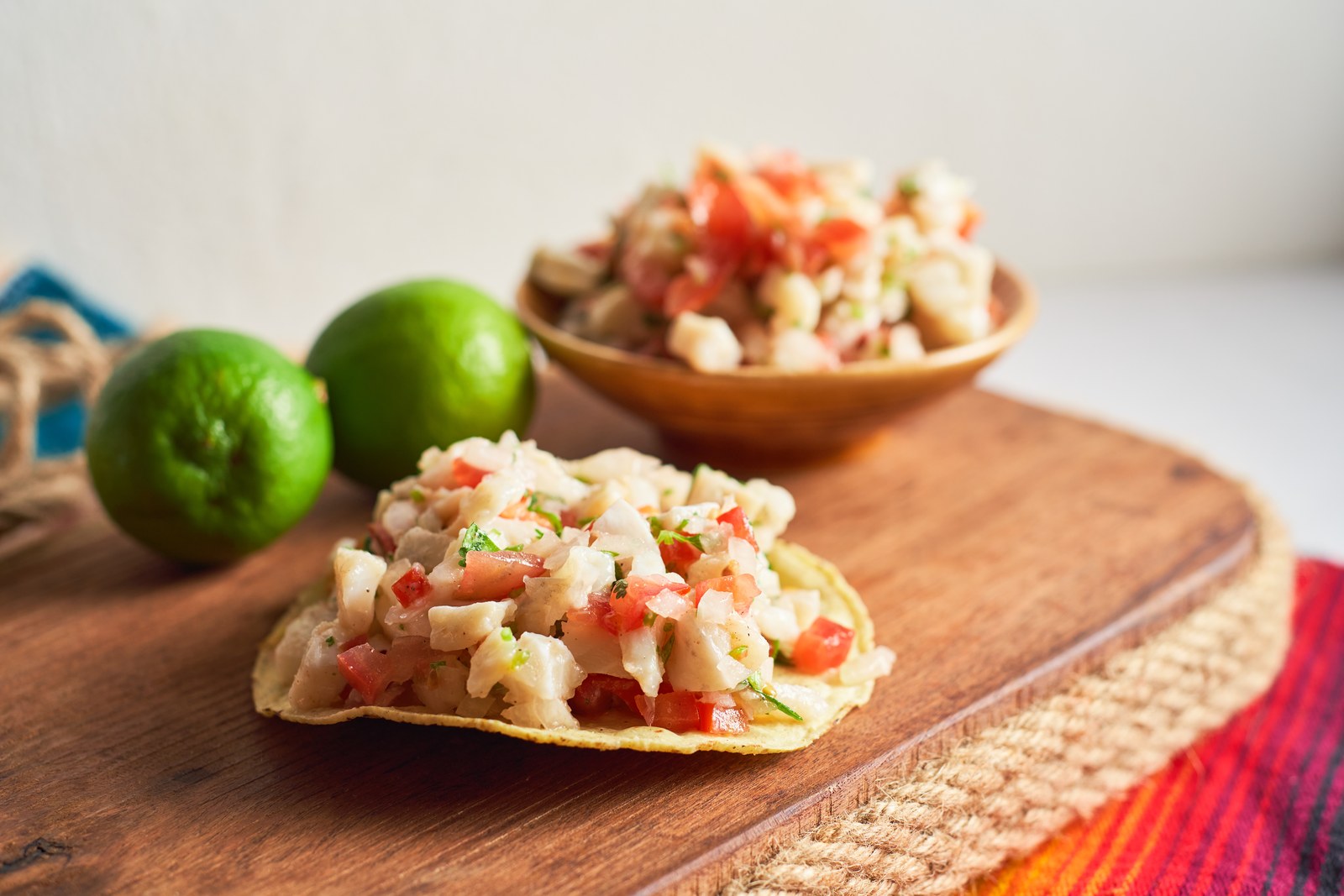 Mexican ceviche tostadas on crispy corn tortillas topped with fresh white fish, diced tomatoes, cilantro, red onions on rustic wooden board with fresh limes