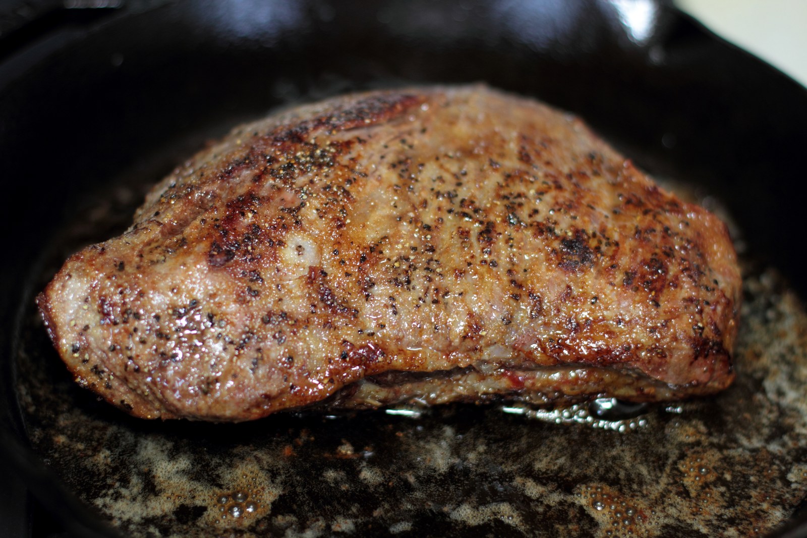 Reverse seared tri-tip beef roast with deep brown crust, coarse black pepper, golden-brown exterior resting on dark granite surface
