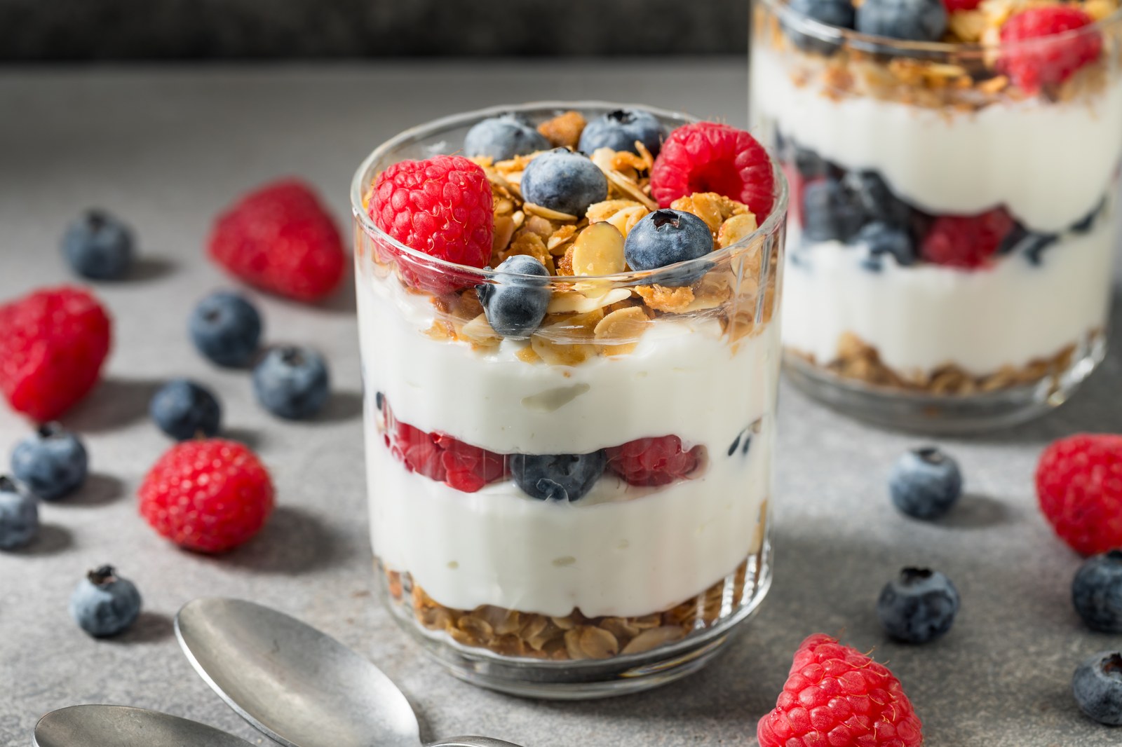Layered yogurt parfait with creamy white yogurt, crunchy granola, fresh blueberries, raspberries in clear glass showing distinct layers